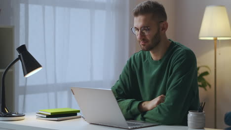 Online-Kommunikation-Per-Video-Chat.-Junger-Mann-In-Grünem-Sweatshirt-Und-Brille-Schaut-Auf-Das-Display-Seines-Notebooks-Und-Nickt-Mit-Dem-Kopf,-Porträtaufnahme-Im-Wohnzimmer